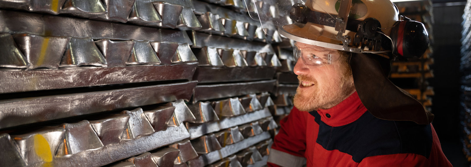 a man wearing a hard hat next to a stack of aluminium billets